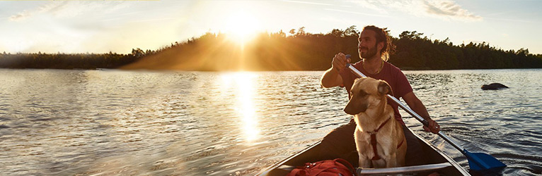 Mann paddelt mit Boot und Hund über den See