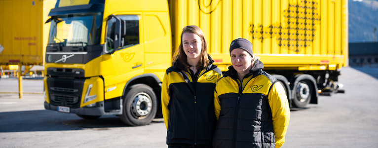 Zwei Frauen stehen nebeneinander vor einem gelben LKW der Post